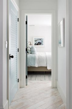 white washed wood floors lead past a blue louvered closet door to a bedroom fitted with
