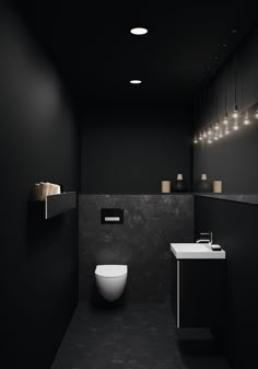 a black and white bathroom with lights hanging from the ceiling over the toilet, sink and mirror