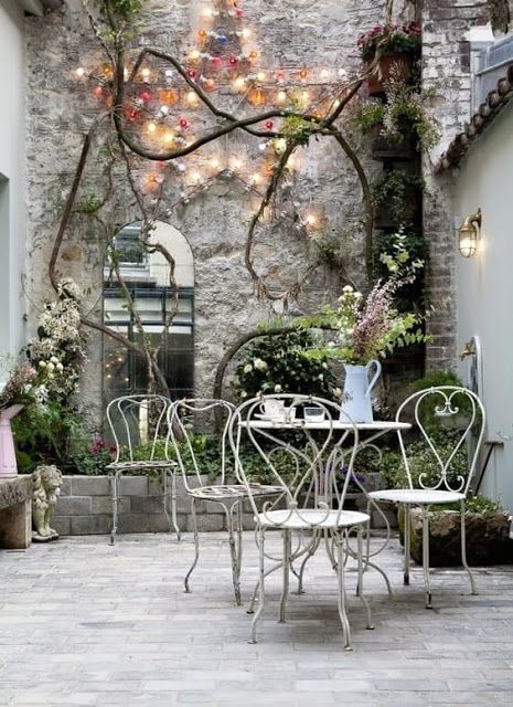 French farmhouse decor and French Country style inspiration from this Paris courtyard with stone wall, fairy lights, mirror, and bistro furniture. #parisdecor #frenchcountrydecor #frenchfarmhouse #frenchcourtyard #patiodecor #outdoordecor #gardeninspiration