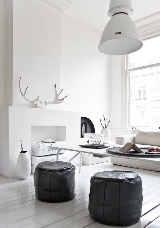 Scandinavian modern style room with stark white walls, black ottomans, and glossy white wood floors. Antlers on fireplace and #rusticdecor