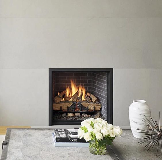 A grey fireplace surround, which travels from the floor to the ceiling, contrasts the black frame and dark brick of the fireplace