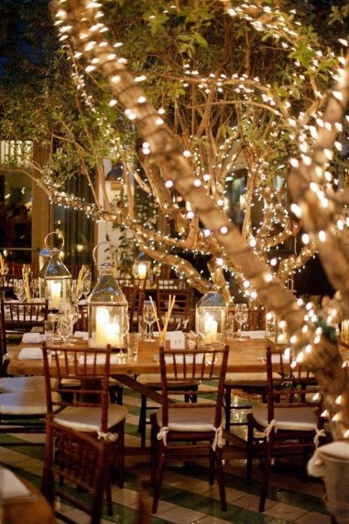 Beautiful trees wrapped in fairy white lights and lanterns on tables.Romantic Wedding Lighting Ideas #weddinginspiration