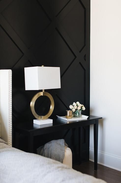 A Gold Ring Lamp Sits On A Black Console Table Placed In Front Of A Black Paneled Accent Wall Beside A Lig Black Accent Walls Accent Wall Bedroom Bedroom Decor