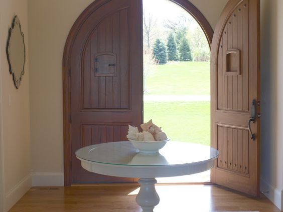 Custom Andean walnut arched double doors with speakeasies/Serene and timeless entry in European country house with Nordic French style/foyer/round table with bowl of conch shells/Venetian mirrors/white oak flooring/Hello Lovely Studio