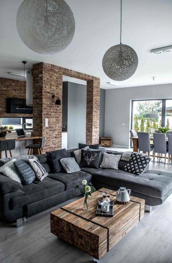 Un salón y cocina abiertos. La pared de ladrillo envejecido y la madera contrastan con el frío de los tonos del suelo y mobiliario gris. #home #decor #homeinteriordesigns