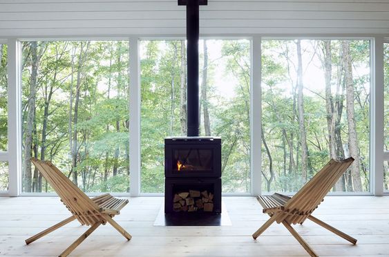 This modern cabin features black fireplace in front of large windows with tree views. #Fireplace #Windows #ModernCabin