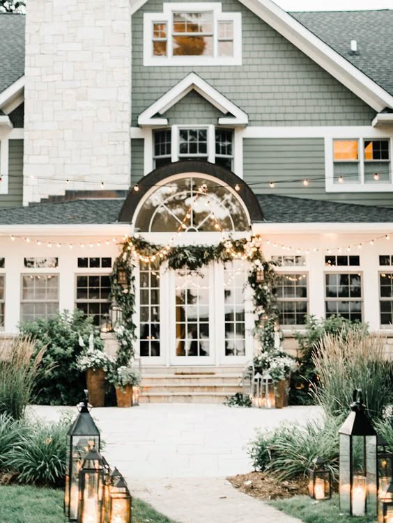 Green shingle style house decked out for Coastal Christmas with garland and lanterns