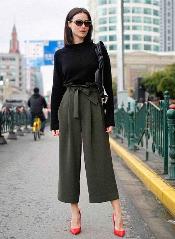 Lena Lademann usa calça clochard com tricot preto e scarpin vermelho.