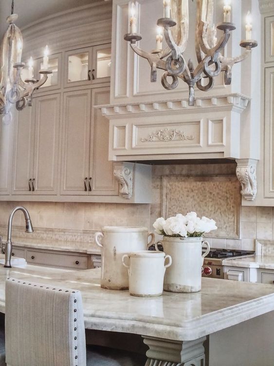 Serene kitchen decor in a French Country kitchen with romantic chandeliers, French pots, and magnificent cabinetry. #frenchcountry #kitchendecor #kitchendesign #chandeliers #whitekitchen #serene #timeless #oldworld #luxurykitchen #greykitchen