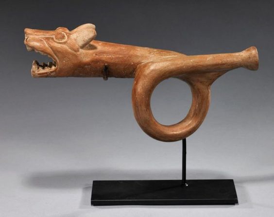 North Coast Peru, ca. 300-500 CE. Large orange-brown glazed terracotta trumpet with cream-colored highlights depicting a ferocious, open-mouth jaguar head with large fangs.