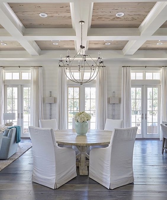 Gorgeous coffered ceiling in dining room with beachy, coastal, traditional style decor. The white slipcovered dining chairs around the rustic round table are so welcoming! #diningroom #beachhouse #cofferedceiling #coastaldecor #traditionaldecor