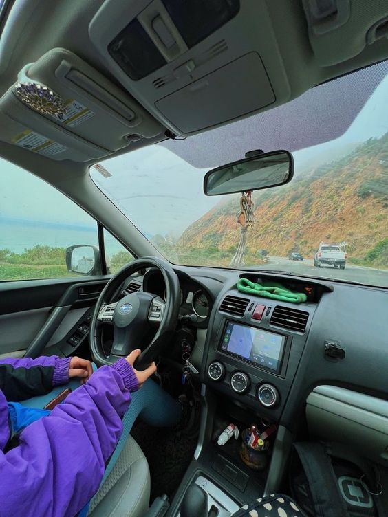passenger seat photo of ocean and road, inside of car decorations, driver curving along road on cliffs driving over ocean