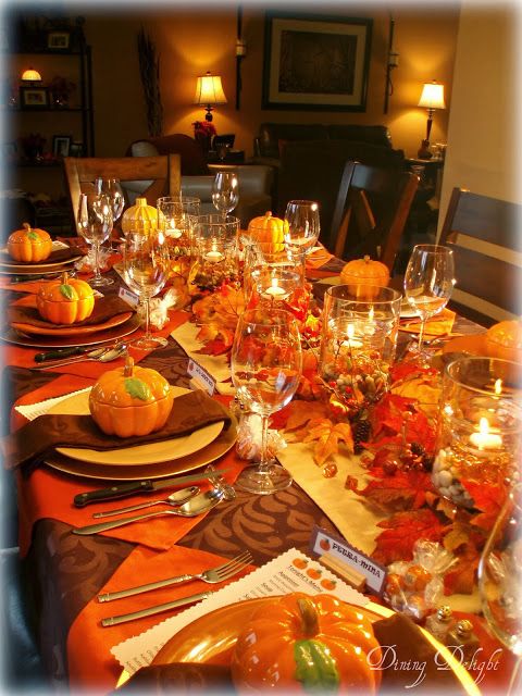 Dining Delight: Fall Dinner Party for Ten. Orange brown yellow. 5 double wall hurricane vase centerpiece. Outside filled with river rocks, inside with orange gems, water, floating candles. Place setting: gold charger, orange plate, pumpkin tureen. Looks like placemat is orange napkin turned in diamond shape.