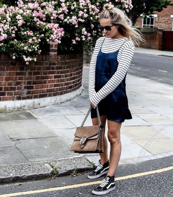 Look lindo e estiloso, com vestido azul de alcinhas em cima de blusa listrada de manga longa, bolsa e tênis