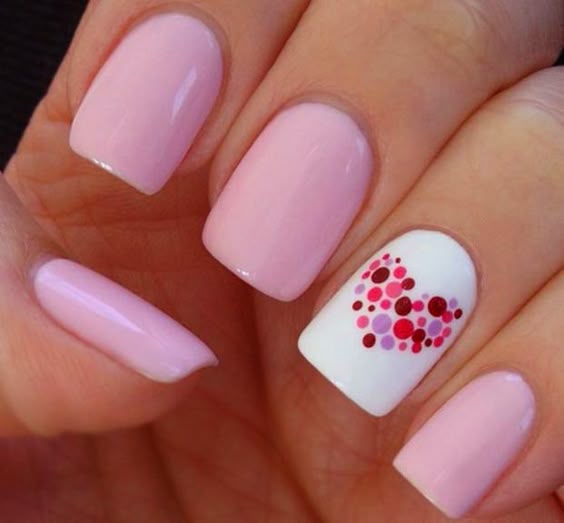 Uñas decoradas con esmalte color rosa y un corazón hecho con puntos de colores