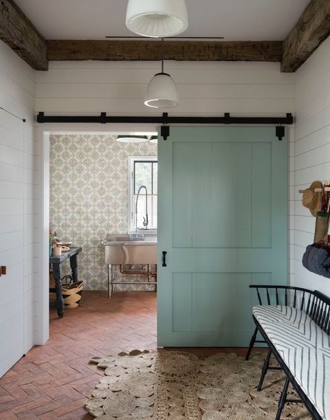 Beautiful modern farmhouse by Jennifer Bunsa with sliding Shaker style barn door, shiplap, rustic wood beams, herringbone tile floor, and industrial freestanding stainless sink. #modernfarmhouse #barndoor #mudroom