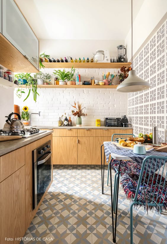 Cozinha com parede de tijolinhos e cobogós tem azulejos hidráulicos, armários de marcerania, plateleiras com vinhos e plantas, iluminação pendente, bancada de cimento queimado, cadeiras spaghetti e mesa de café | colorful, simple and cozy decor in a renovated apartment with modern touches and preserved old architecture. (In Portuguese)