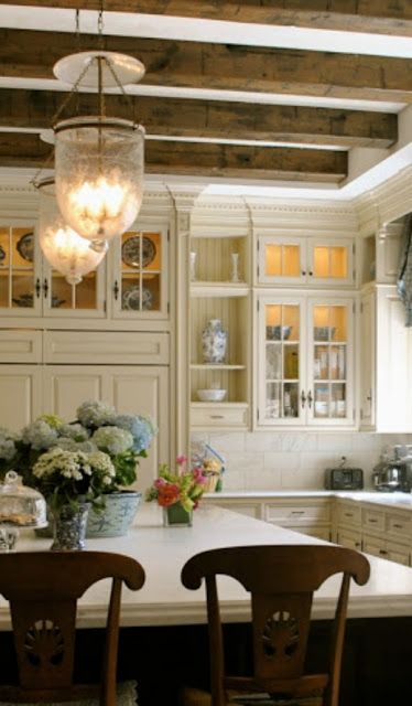 White kitchen ideas in photos we can't stop pinning! Elegant French inspired white kitchen with white cabinets, large black painted island, bell jar lighting, blue and white porcelain accessories, and stone flooring. Design by The Enchanted Home. #whitekitchen #frenchcountry #belljar #traditional