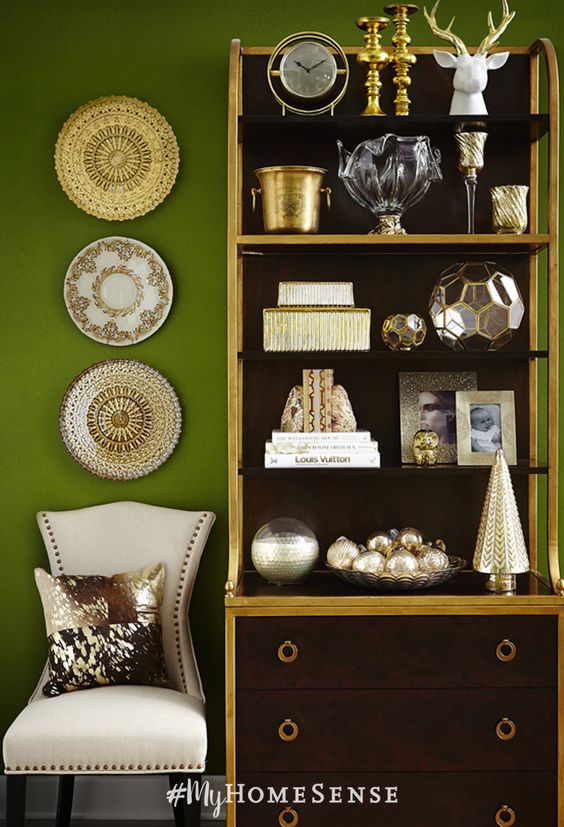 stylist tip: a cohesive colour theme gives a shelving display sophisticated style. Here, the white and gold accessories pop against the dark wood bookshelf and moss green walls.