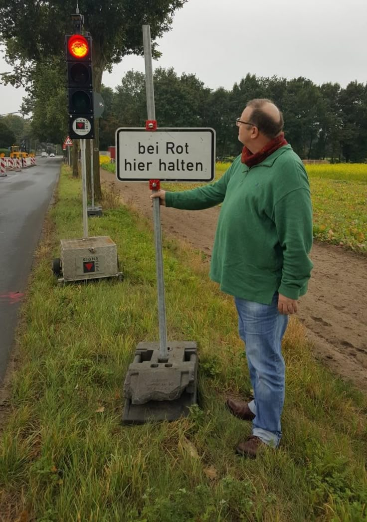 a man standing next to a traffic light with a sign on it that says, bei rot her halten