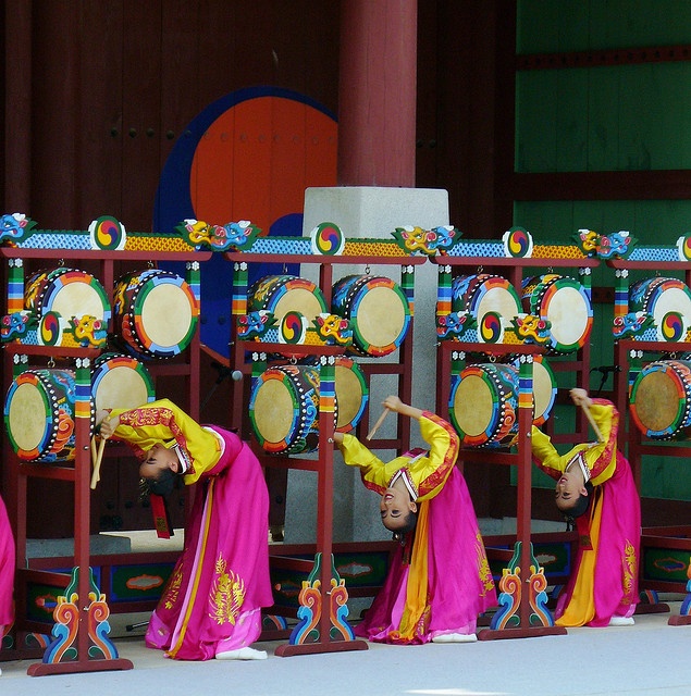 several people in colorful costumes are performing on stage with musical instruments and drum stands behind them