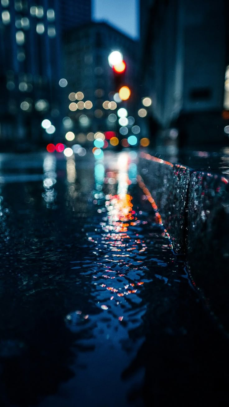 rain drops on the ground in front of a city street at night with buildings and traffic lights