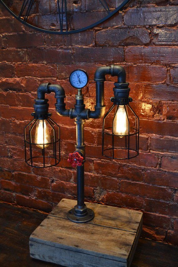 a lamp made out of pipes and light bulbs on a wooden block in front of a brick wall