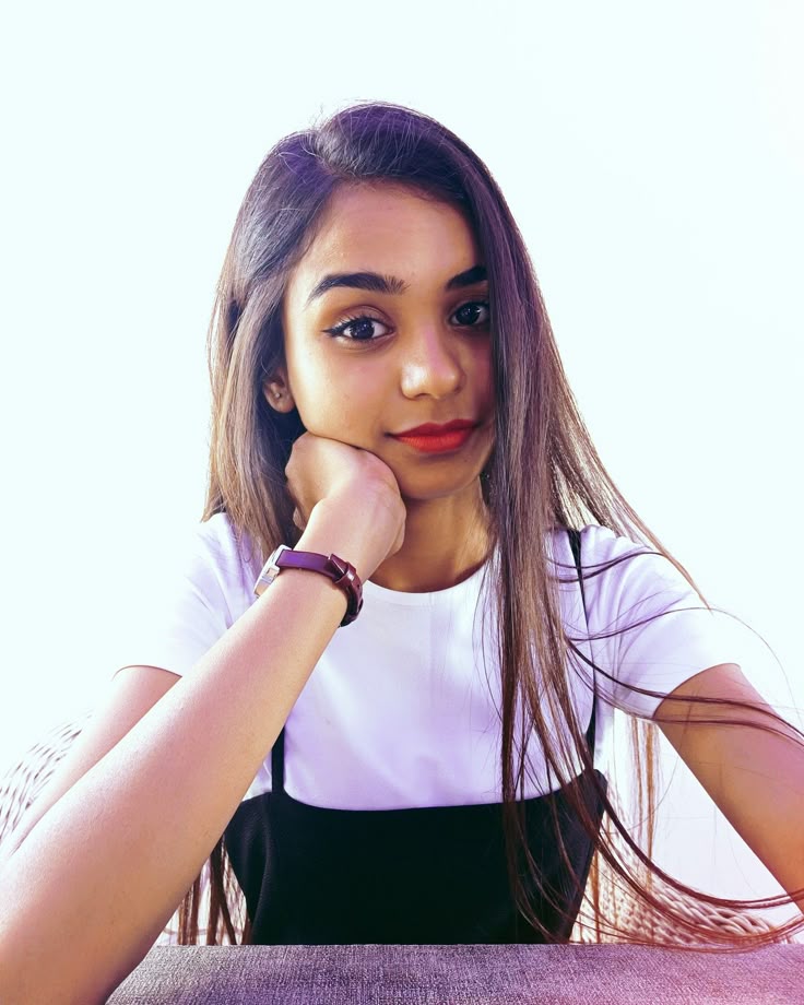A Woman Sitting At A Table With Her Hand On Her Chin And Looking To The a-woman-sitting-at-a-table-with-her-hand-on-her-chin-and-looking-to-the