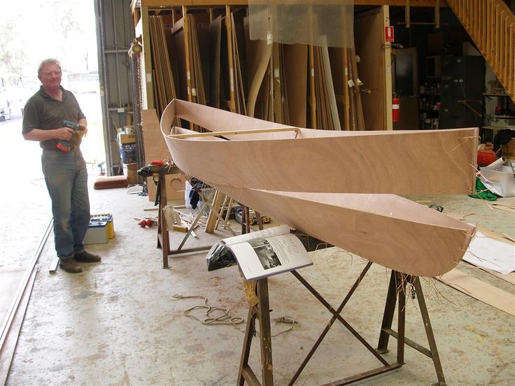 a man standing next to a wooden boat in a shop with other woodworking tools