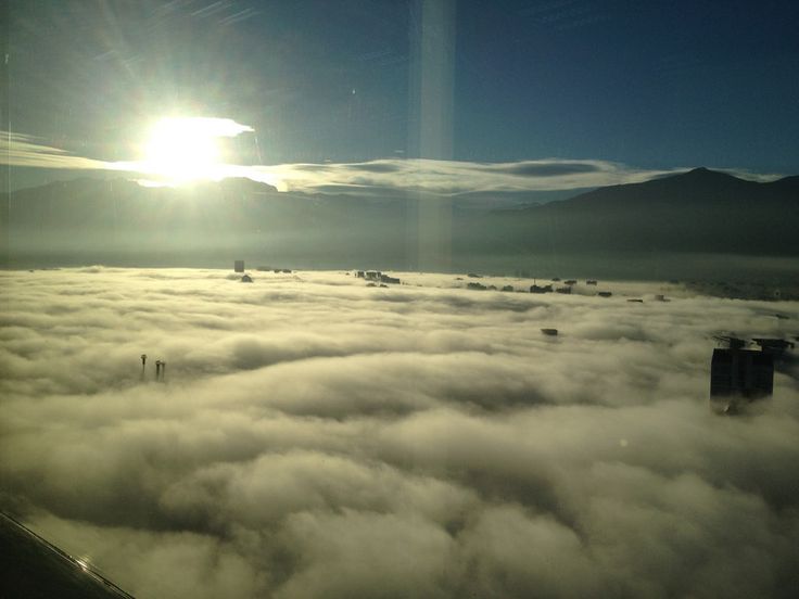 the sun is shining over some clouds in the sky with buildings and mountains behind it