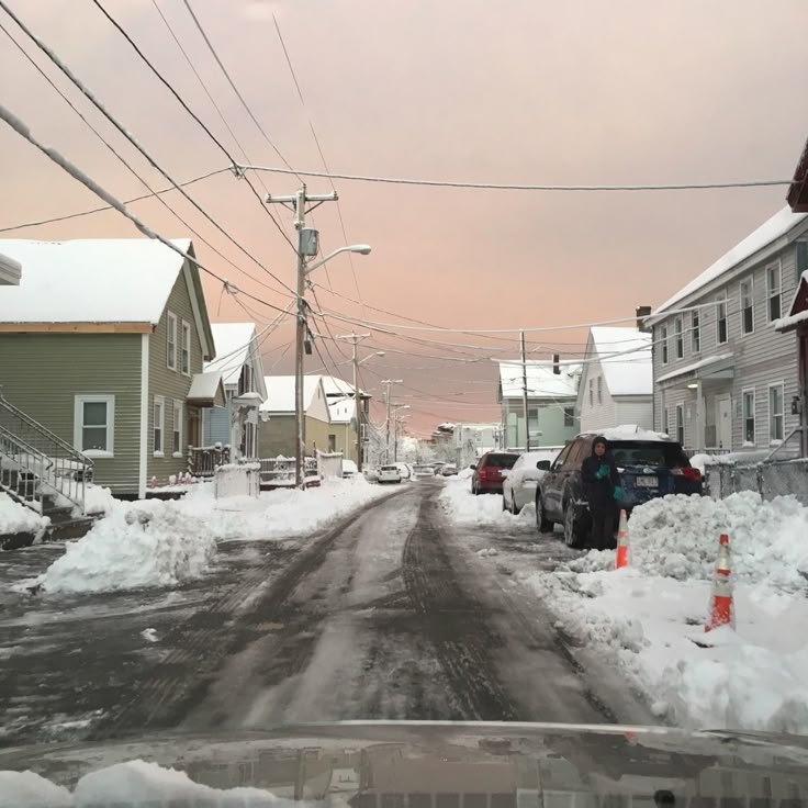 cars parked on the side of a snow covered road in front of houses and power lines