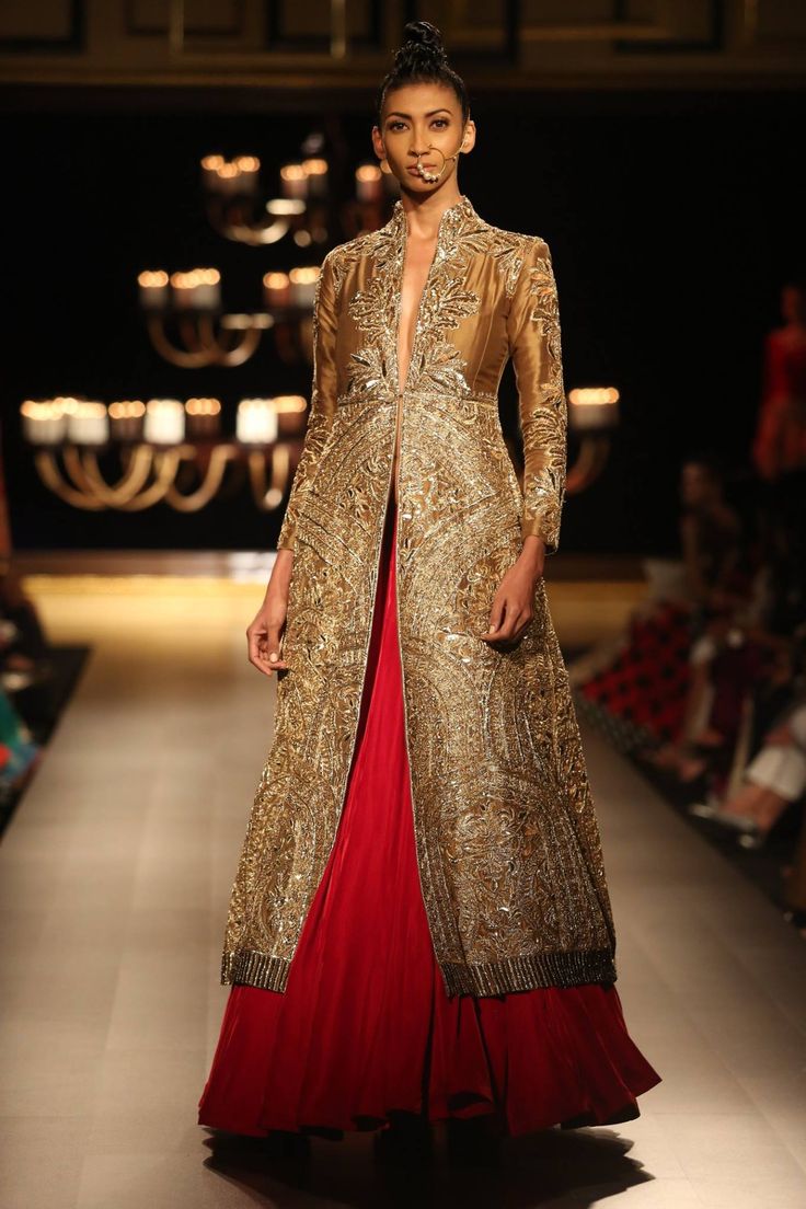 a model walks down the runway in a gold and red outfit