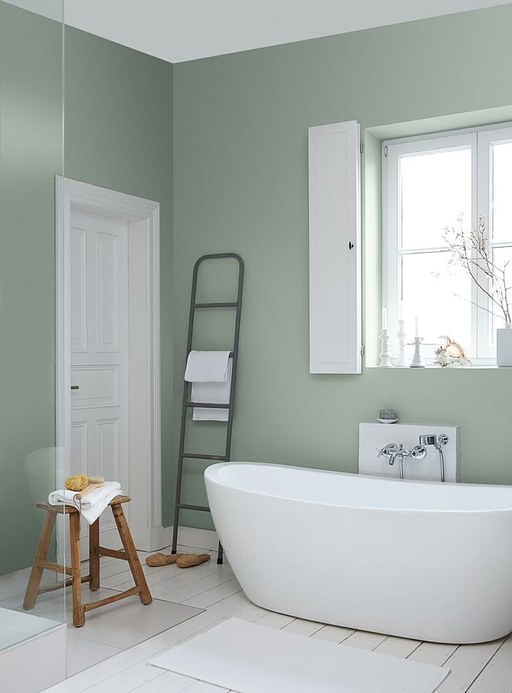 a white bath tub sitting under a window next to a ladder in a green bathroom