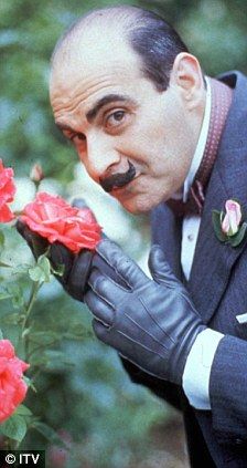 a man with a moustache on his face is smelling some red roses in front of him