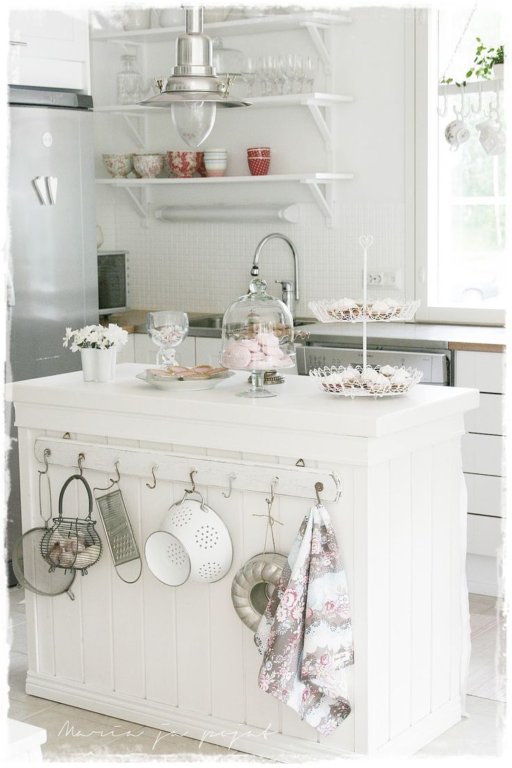 a white kitchen with pots and pans hanging on the wall above an island counter