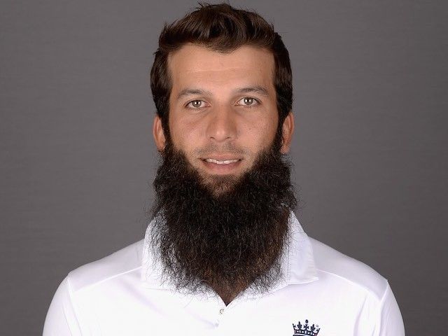 a man with a long beard wearing a white cricket uniform and holding a ball in his hand