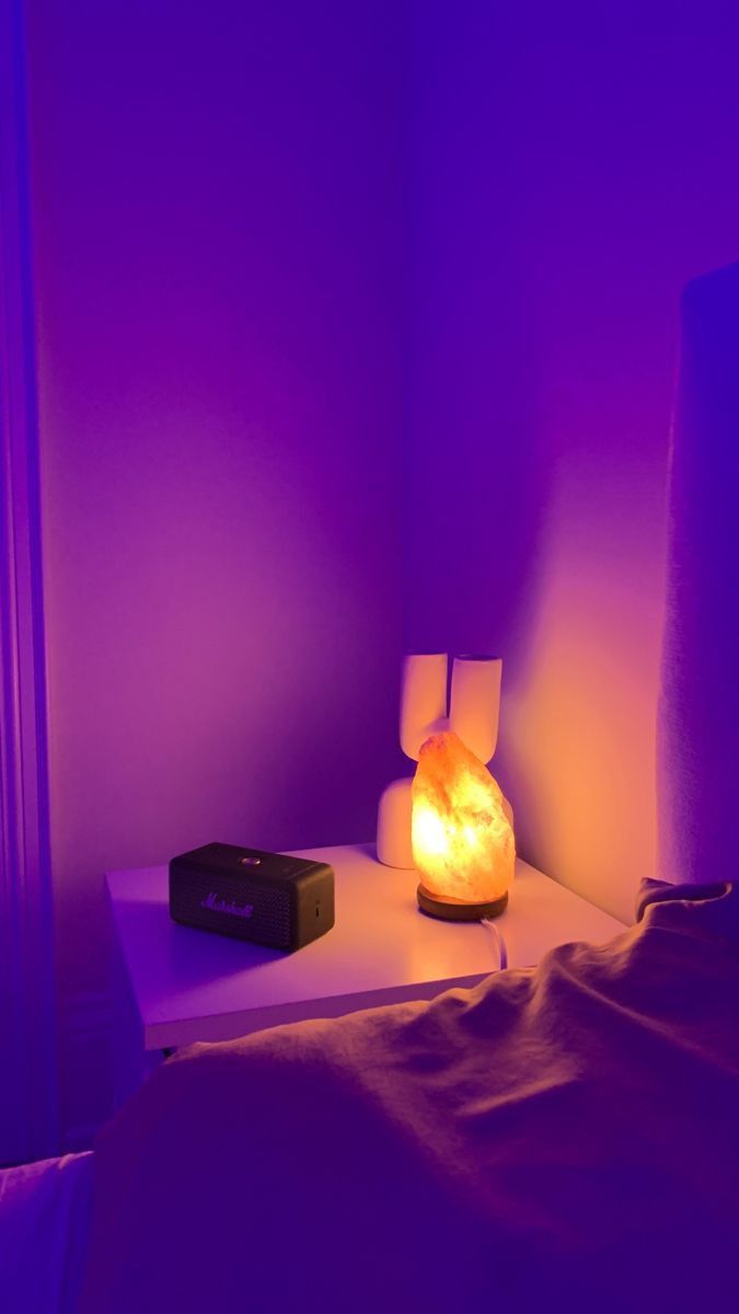 A Night Stand With A Lamp On It Next To A Bed In A Purple Room a-night-stand-with-a-lamp-on-it-next-to-a-bed-in-a-purple-room