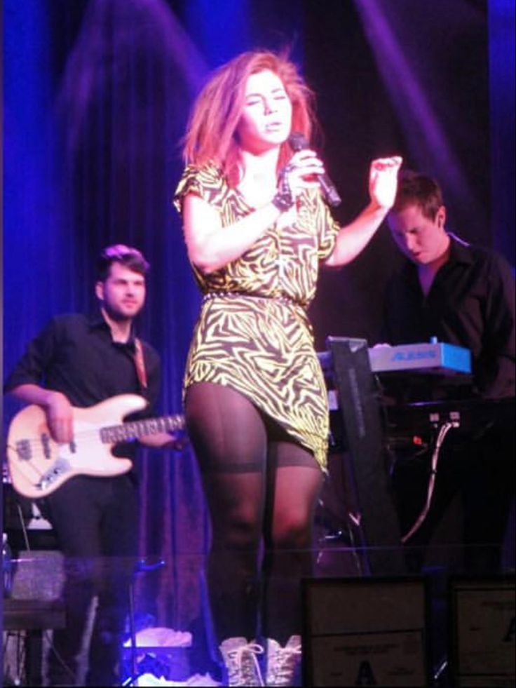 A Woman In Tights On Stage Singing Into A Microphone And Two Men a-woman-in-tights-on-stage-singing-into-a-microphone-and-two-men