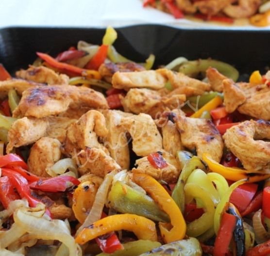 chicken fajita with peppers and onions in a black skillet on a white tablecloth