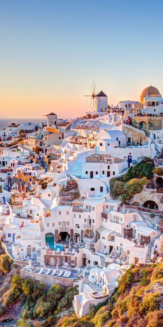 an aerial view of the white city of oia, with windmills in the background