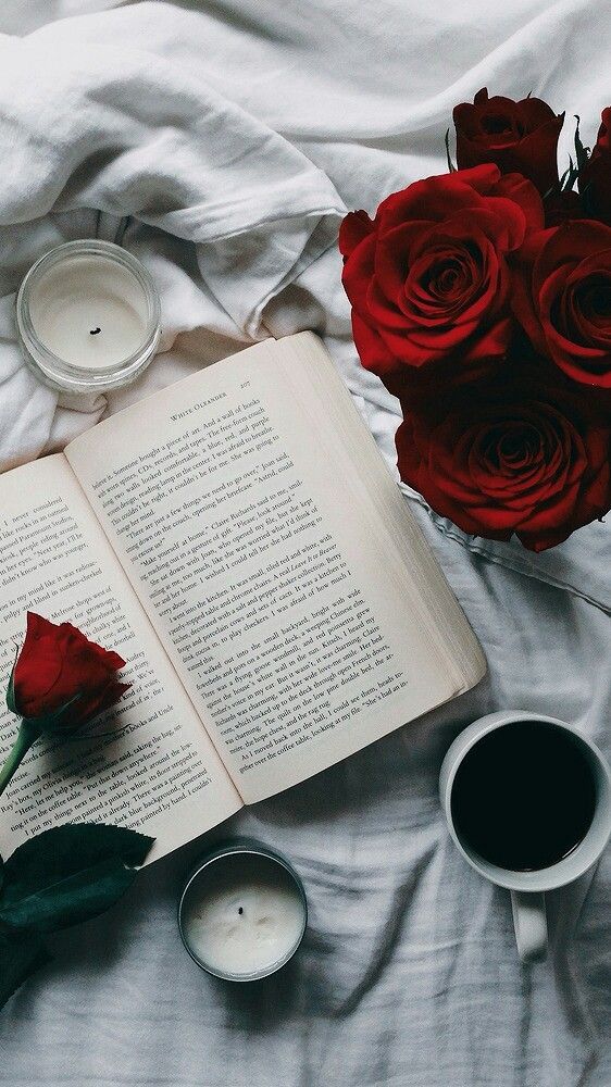 an open book and some candles on top of a bed with red roses next to it