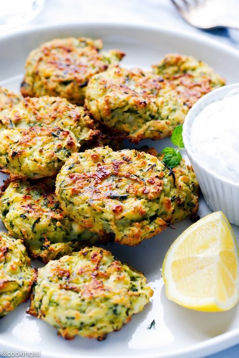 several crab cakes on a white plate with a small bowl of ranch dressing next to it