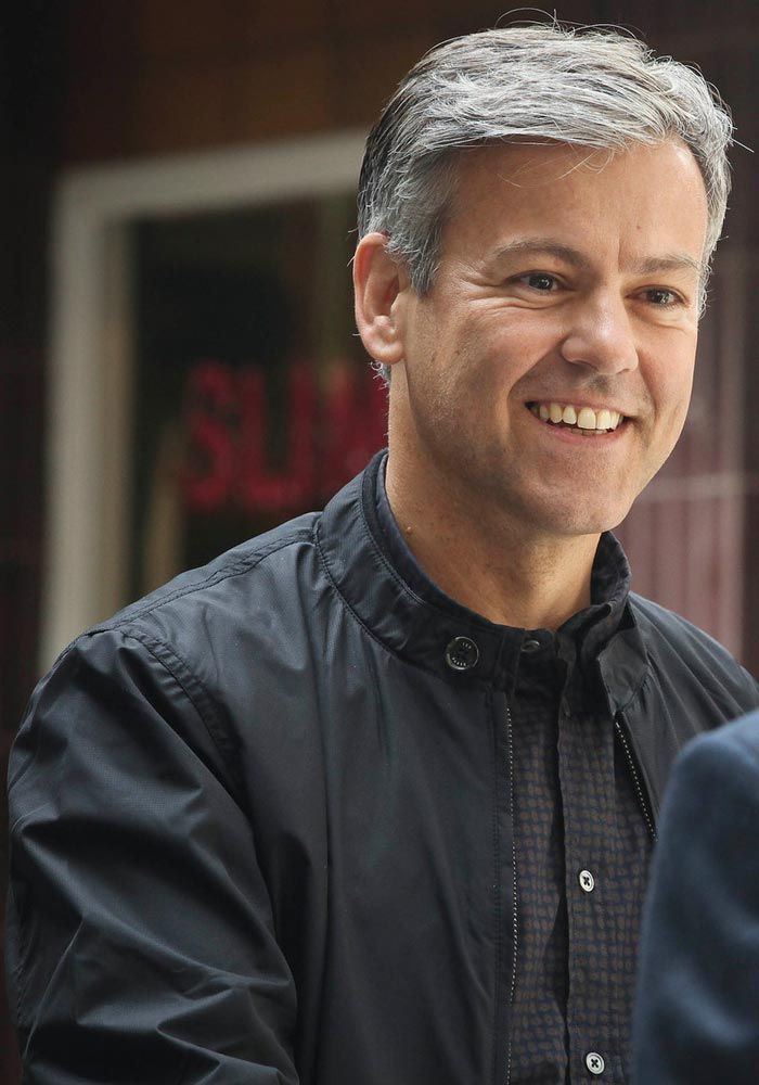 a man in a black jacket smiles at the camera