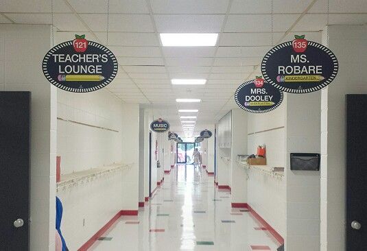 Wow! What an AWESOME transformation! Your RoomTagz hallway signs look great. The principal admitted he was reluctant to purchase the double-sided hallway signs at the suggestion of a few teachers who saw them on Pintetest, but enthusiastically relieved he did because of the difference they make. Each sign is approximately $50 and includes sign, all the vinyl lettering needed to personalize, and hanging hardware. The lettering is easily removable & replacable when a change in staff occurs!