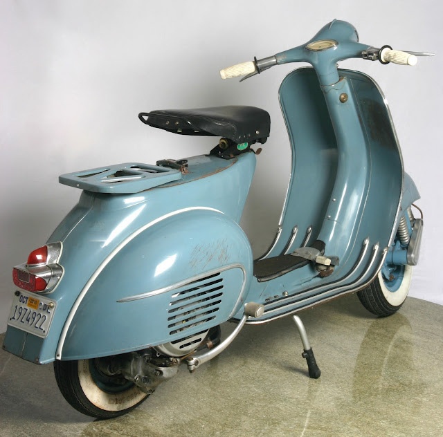 an old blue scooter is parked in a room with a white wall behind it