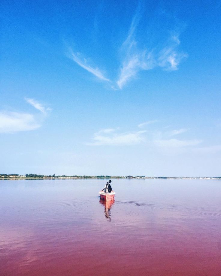 a man riding on the back of a boat across a large body of pink water