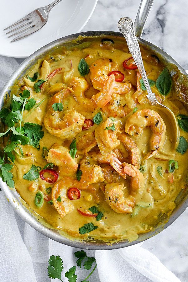 a pan filled with shrimp and vegetables on top of a white table next to silverware