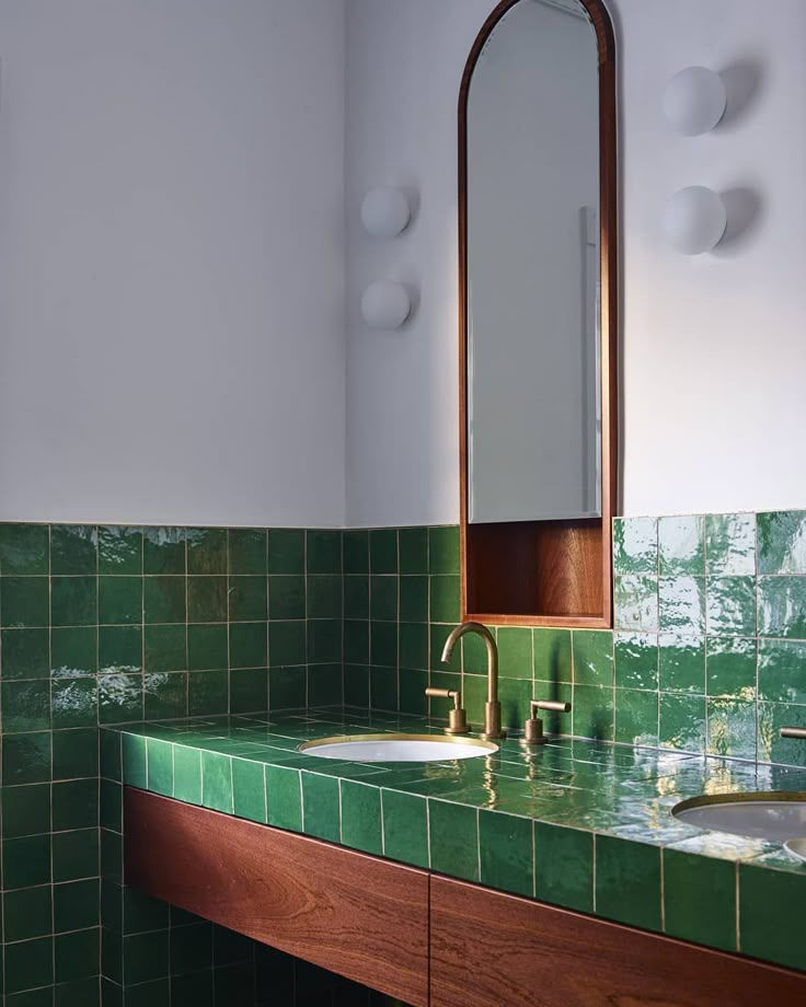 a green tiled bathroom with two sinks and a mirror