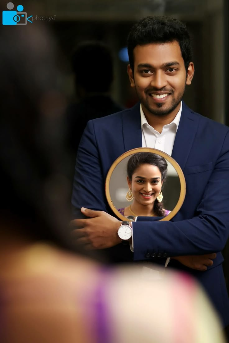 a man in a blue suit holding a mirror with a smiling woman on the other side