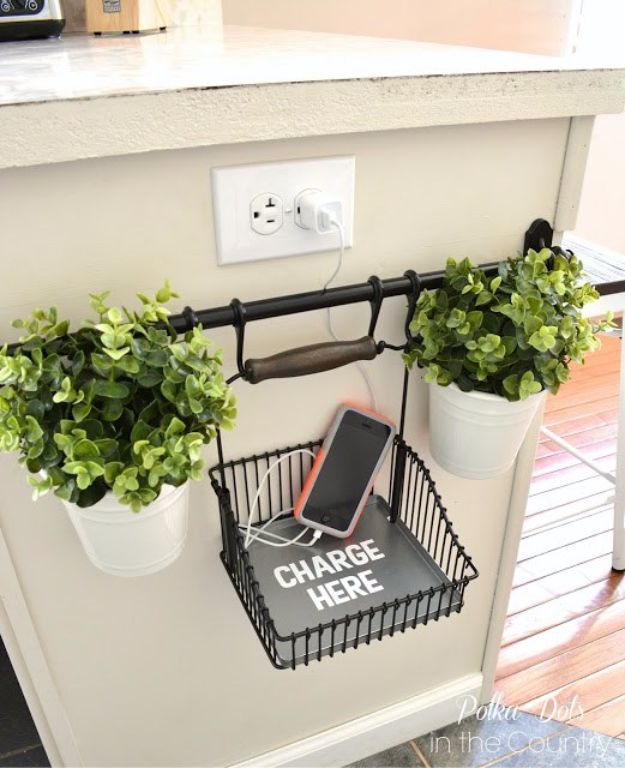 two potted plants and a cell phone are on the shelf in front of an electrical outlet